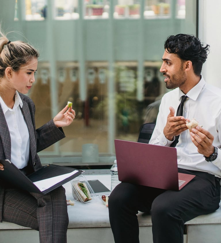 2 people in business meeting while eating sandwich outside with laptop