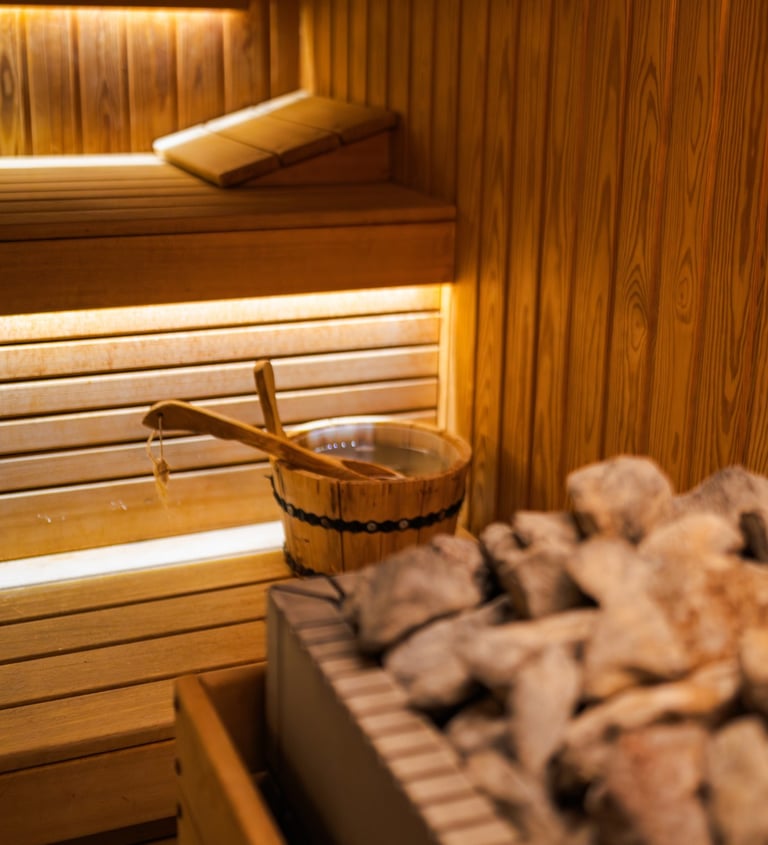 Traditional wooden sauna interior featuring hot stones, a water bucket, and a wooden ladle.