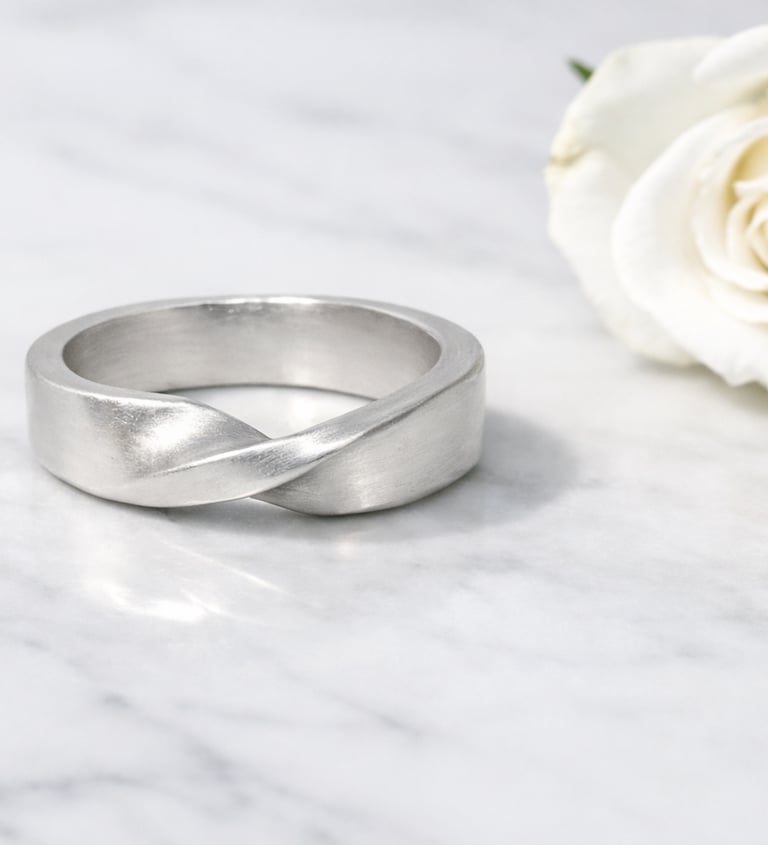 A satin 999 fine silver twisted mobius ring rests on a white marble surface with soft gray veining, 