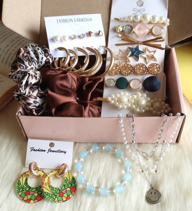 A collection of fashion accessories including gold hoop earrings, pearl hair clips, silk scrunchies, and a smiley face
