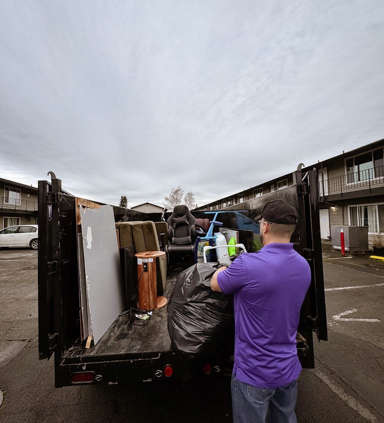 A junk removal professional loading a black dump trailer with furniture and debris for disposal.