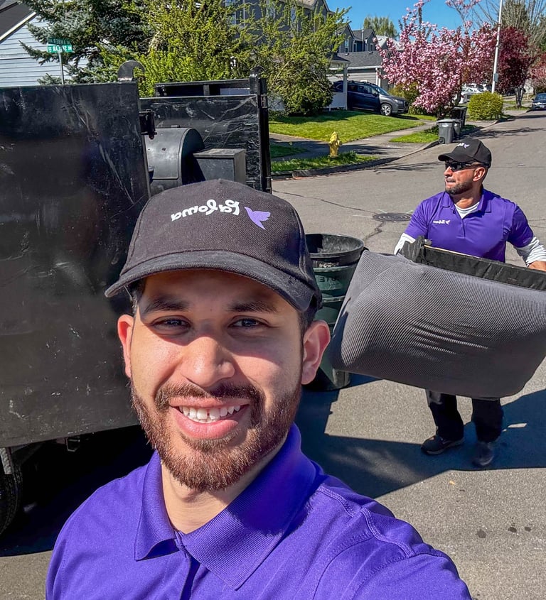 Professional junk removal team loading a mattress into a truck on a sunny residential street.