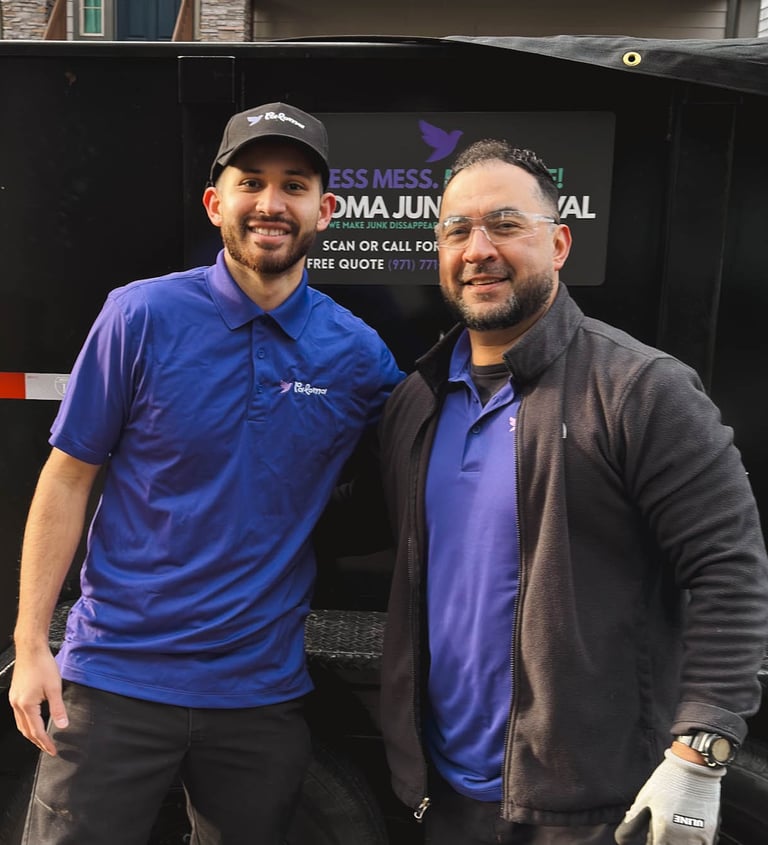 Two professional junk removal specialists standing by a black dumpster trailer.