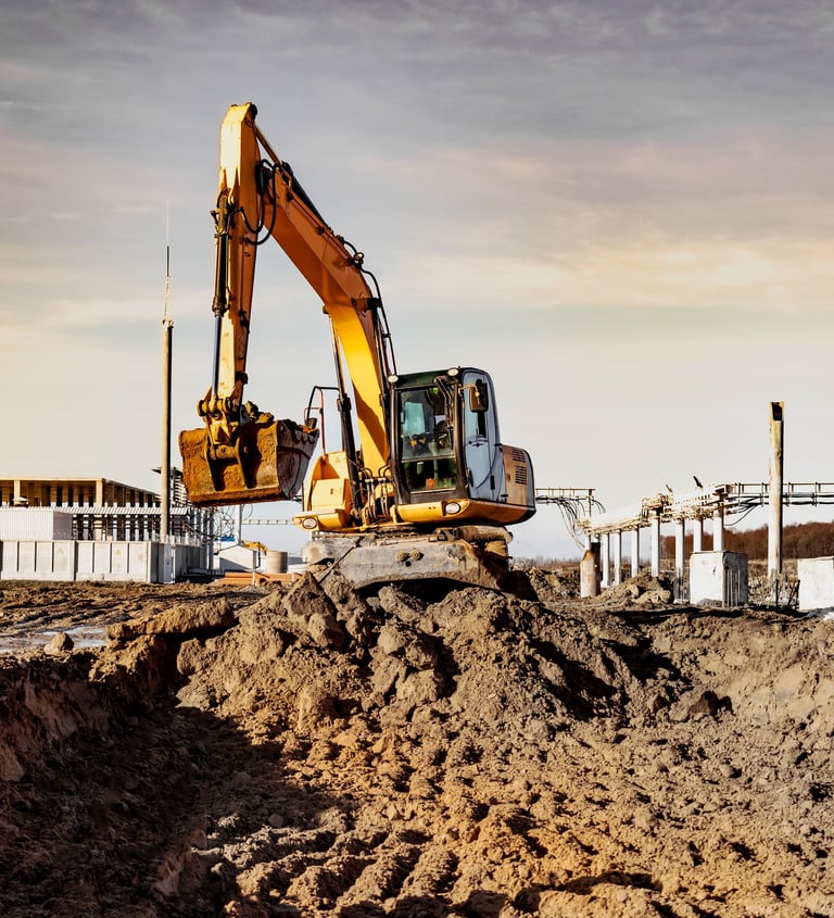 Bagger hebt Erde auf einer Baustelle aus bei Sonnenuntergang, im Hintergrund Rohbau und Kranstruktur
