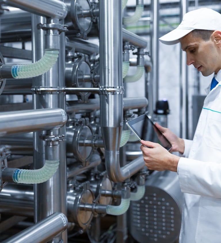 Ingeniero con bata de laboratorio blanca usando una tableta digital para monitorear tuberías industr