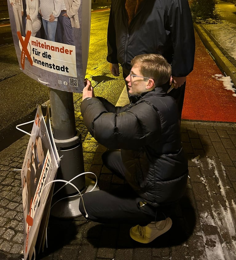 Junger Mann befestigt Wahlplakat an Laternenmast bei Nacht – politisches Engagement