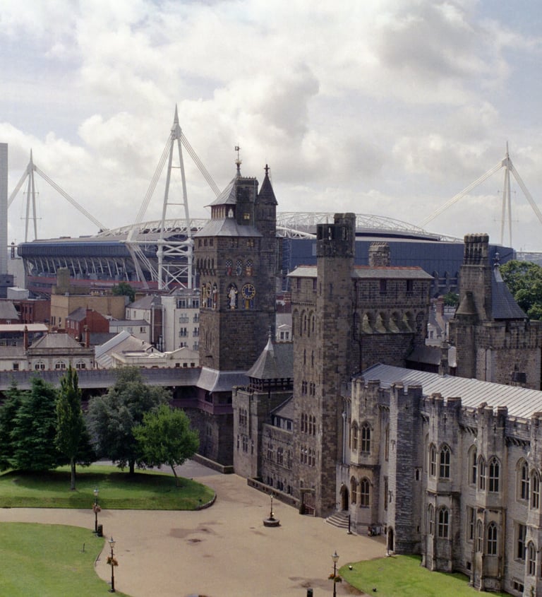 Cardiff Castle grounds featuring historic stone architecture with the modern Principality Stadium in the background.