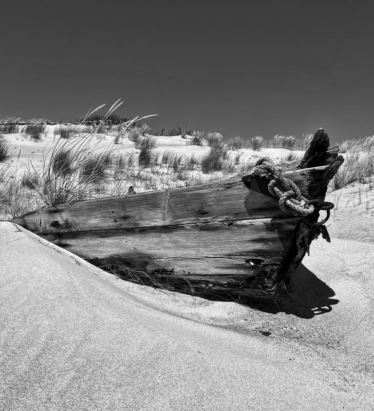 A vintage boat rests on the sandy shore in a black and white photograph