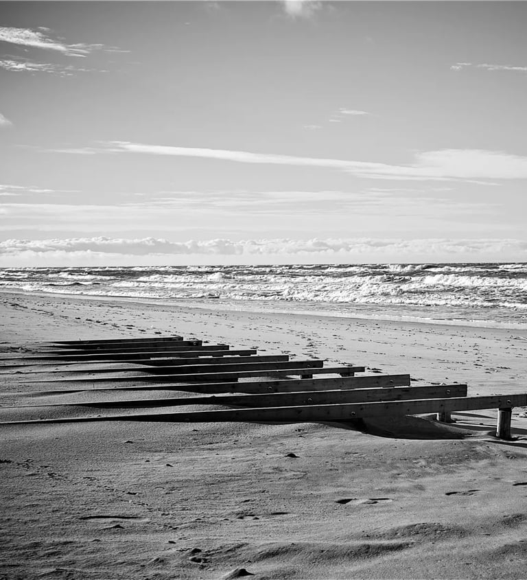 A black and white photo depicting a peaceful beach with wooden benches
