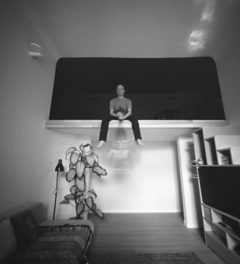 A man sitting in a room, holding cello captured through a pinhole