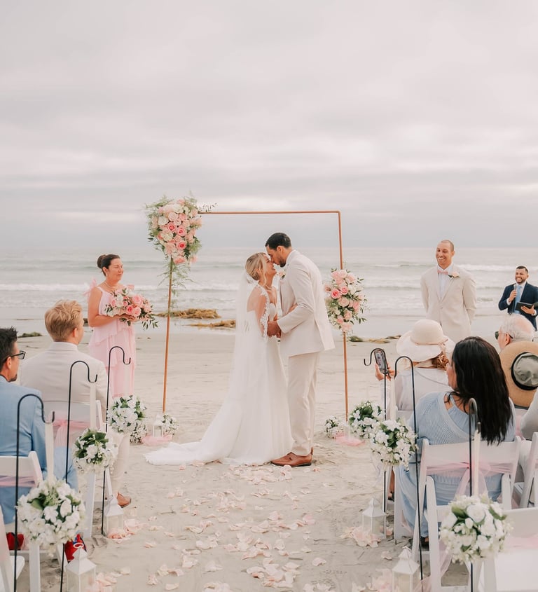 Bride & Groom kissing under arbor pink and white wedding at South Beach, Coronado