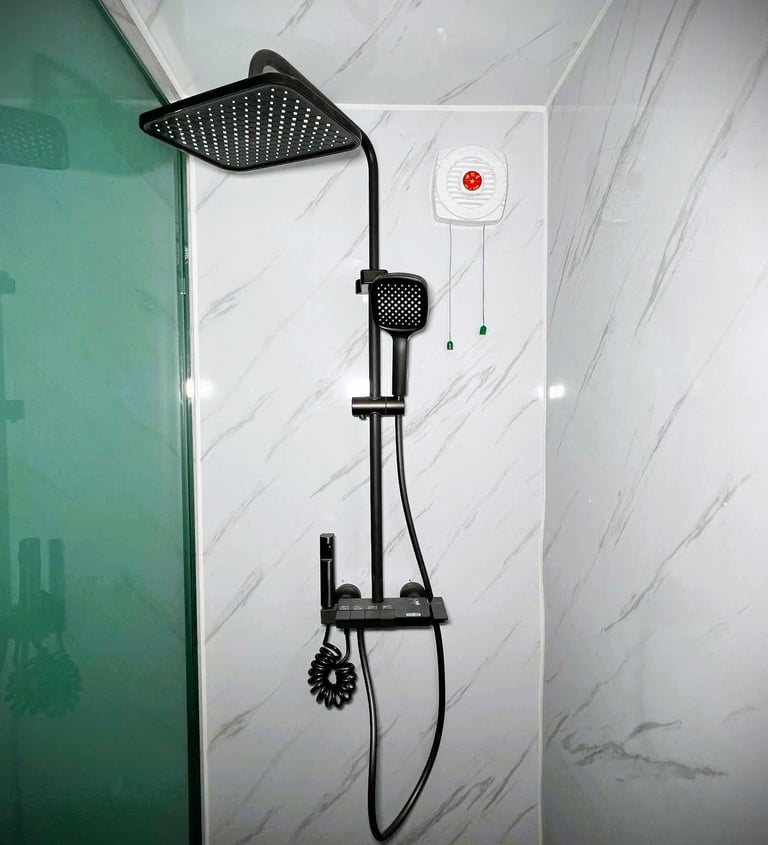 Modern matte black rain shower head system with handheld sprayer and faucet on white marble tile walls.
