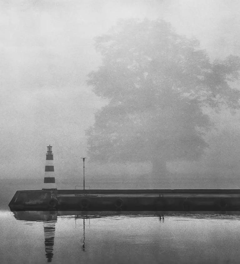 A foggy day captures a black and white lighthouse, emphasizing its silhouette against the misty background.