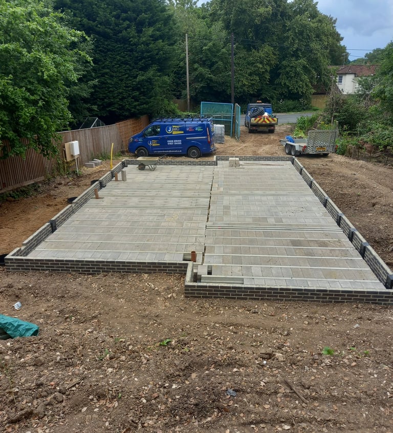 A beam and block floor installation on a new house construction site with work vans in the background.