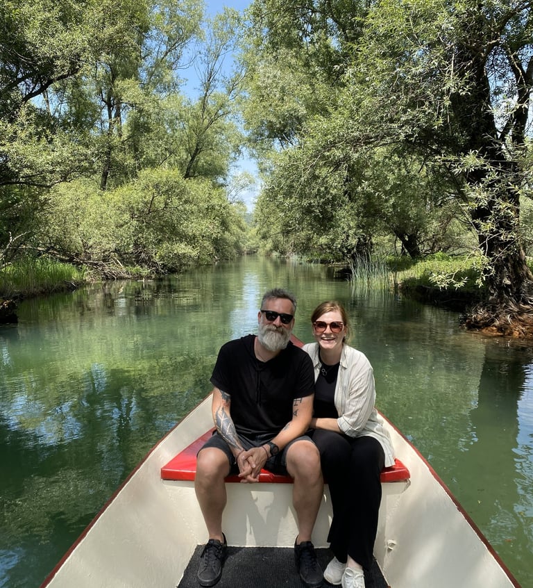 A couple taking a scenic boat tour on a clear green river surrounded by lush summer trees montenegro