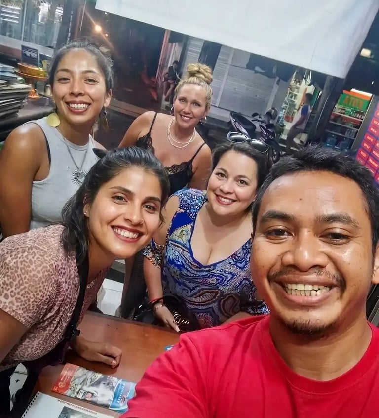 A group of happy diverse friends smiling for a group selfie while dining at an outdoor night market restaurant.