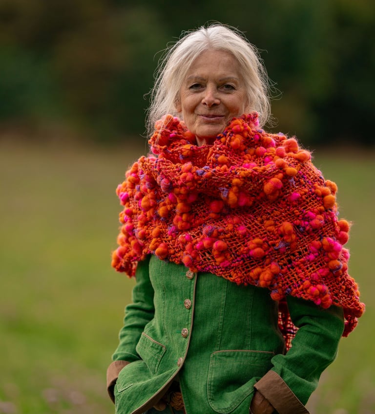 a woman in a green jacket and a red scarf . Triloom gewebter Schal aus Artyarn in orange und pink.