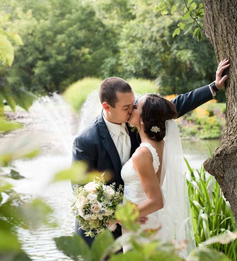 a bride and groom kissing in front of a pond