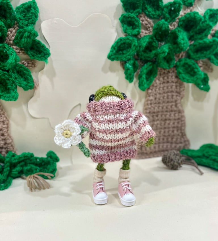 a froggy frog wearing a striped jumper holding a crochet flower