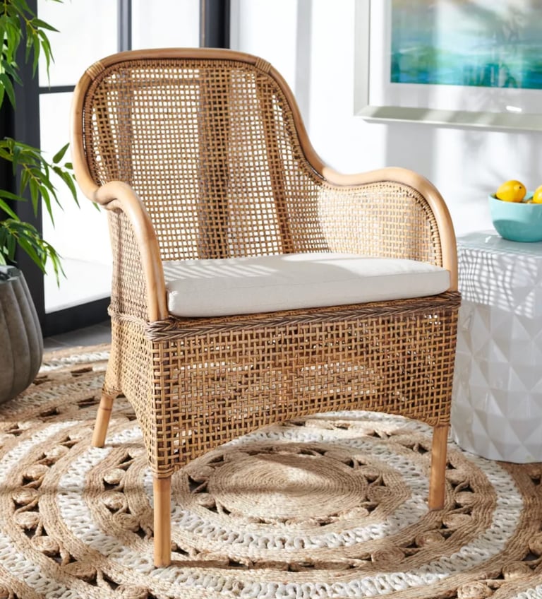 Woven rattan armchair with a white cushion on a round jute rug in a bright living room.
