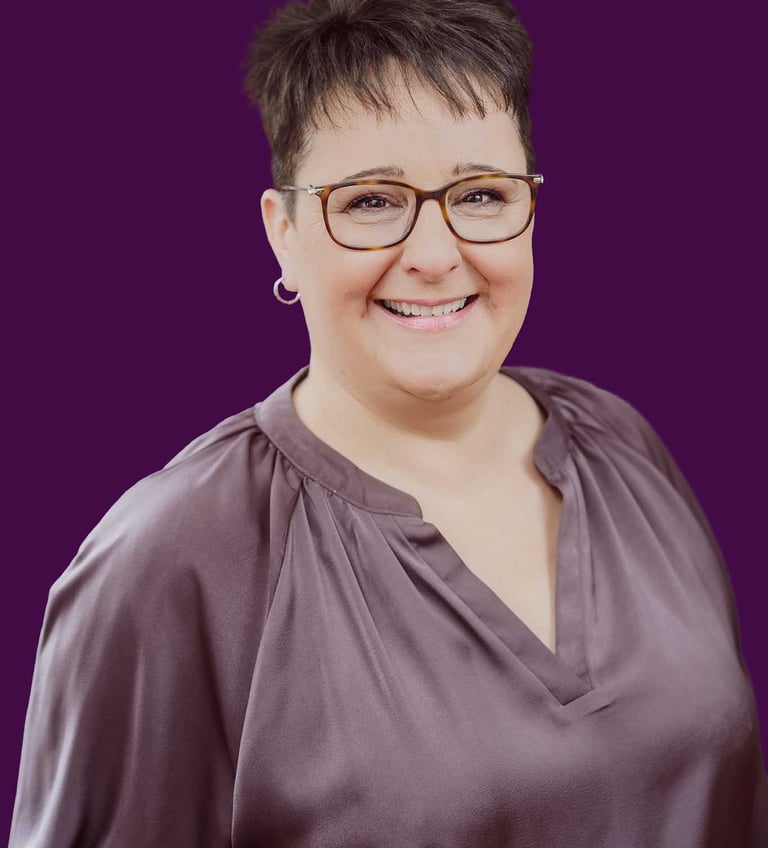 Professional corporate headshot of a smiling woman with glasses and short hair against a purple background.