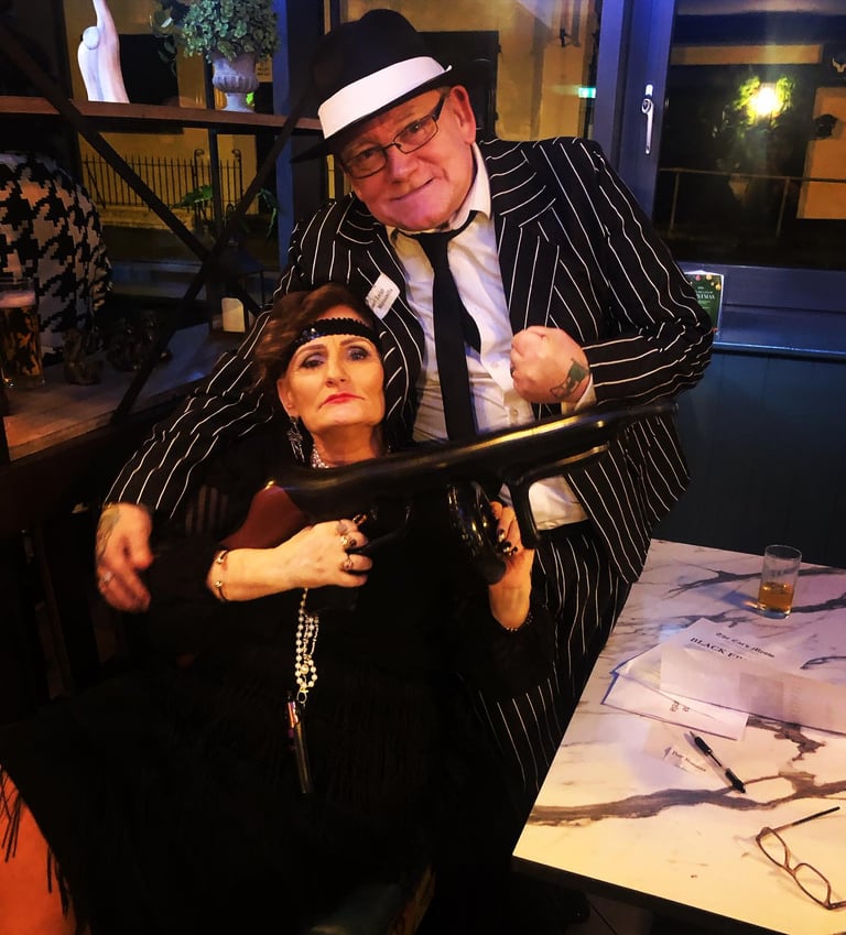 older man and woman at a murder mystery. the woman is holding a gun.