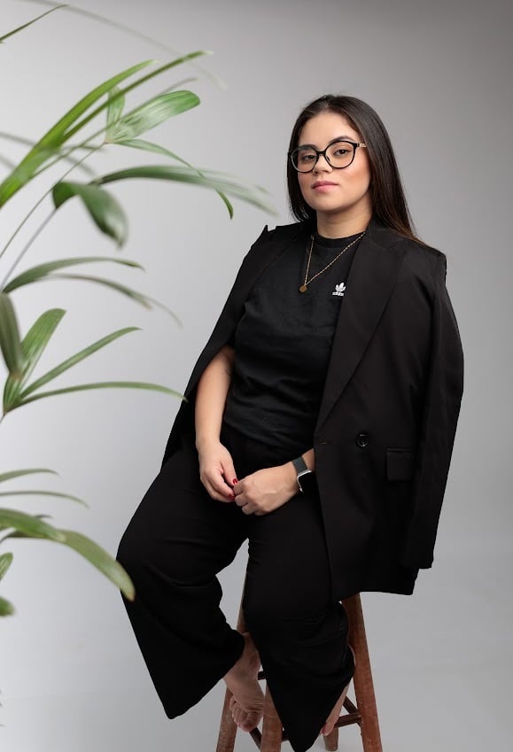 Ensaio de retrato corporativo em Barueri: mulher de óculos com blazer preto, fundo claro com planta
