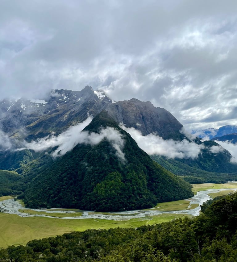 Vista expansiva de montanhas, com um rio, nuvens abraçam a montanha