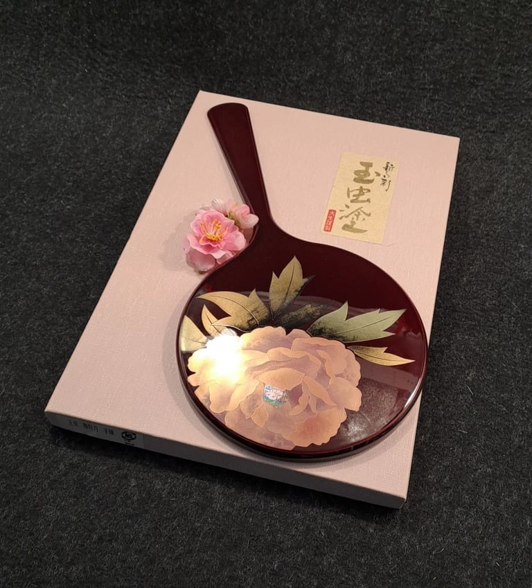 alt="Edler japanischer Handspiegel im Maki-e-Stil mit Blütenmotiv, dekorativ auf rosafarbener Box ar