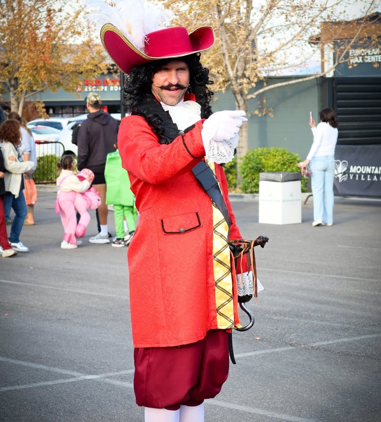 A man in a Captain Hook costume with a red coat and feathered hat at an outdoor event.