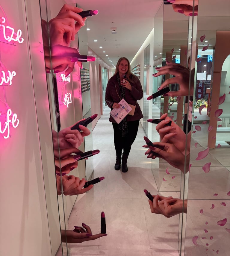 A woman takes a mirror selfie in a creative makeup display corridor with 3D hands holding lipsticks.