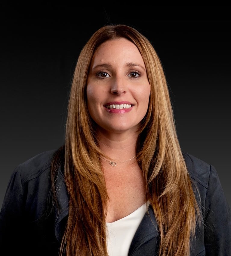 Professional corporate headshot of a smiling Tara Follett with long brown hair wearing a blazer.