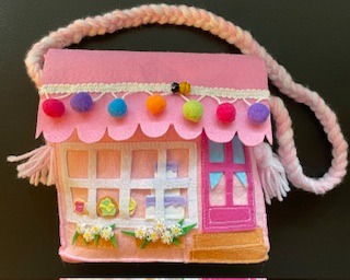 Pink felt dollhouse purse with colorful pom-poms, embroidered windows, and a braided strap, perfect for kids' imaginative