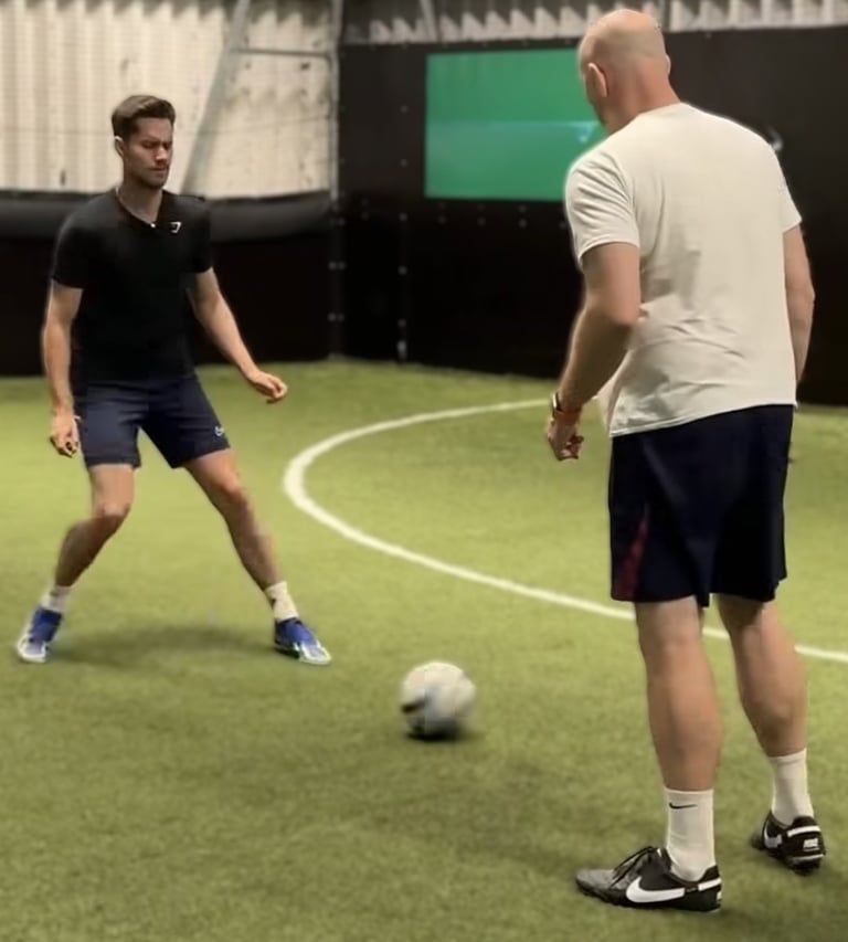 Two people taking part in a football activity on an indoor artificial pitch.