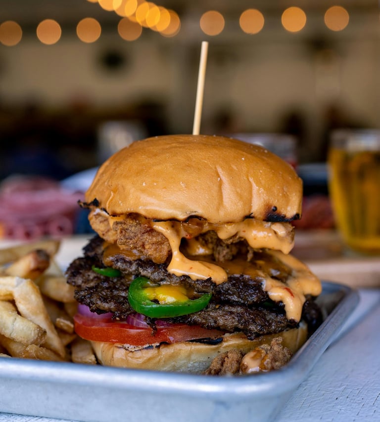 cheeseburger with tomato, onion, jalapeno, and fries on the side, on metal plate
