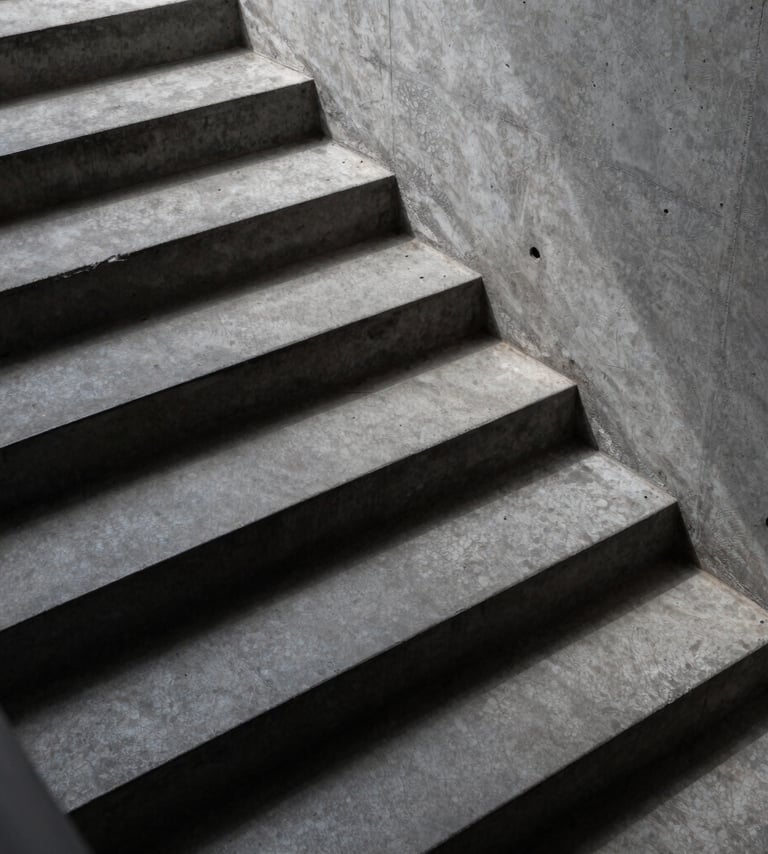 High-angle shot of a minimalist concrete staircase with sharp midnight slate shadows and dusty steel grey surfaces.