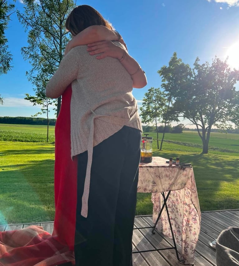 Two friends hugging on a sunny wooden deck overlooking a green field at sunset.