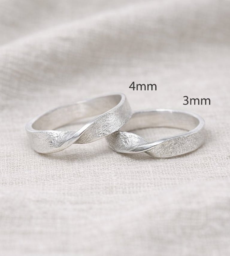 Pair of 999 Fine silver infinity twist wedding bands in 4mm and 3mm widths on linen background.