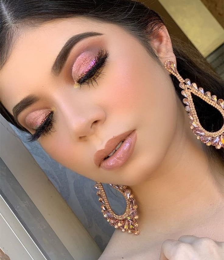 Mujer con sombra de ojos rosa con brillo y aretes colgantes llamativos con gloss labial neutro.