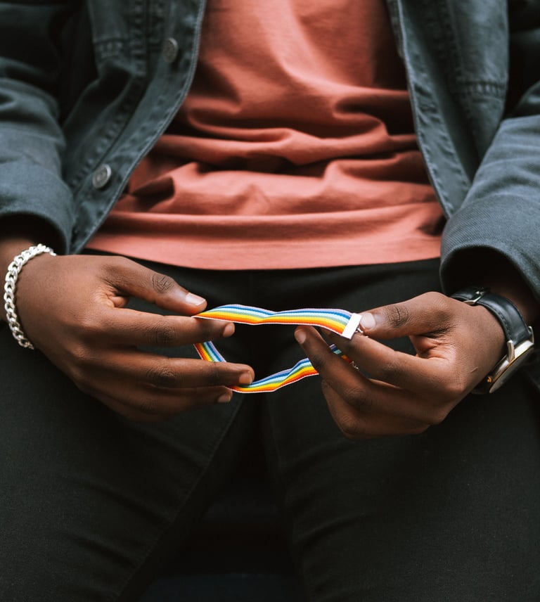A person holding a rainbow pride wristband, representing LGBTQ+ identity and diversity.