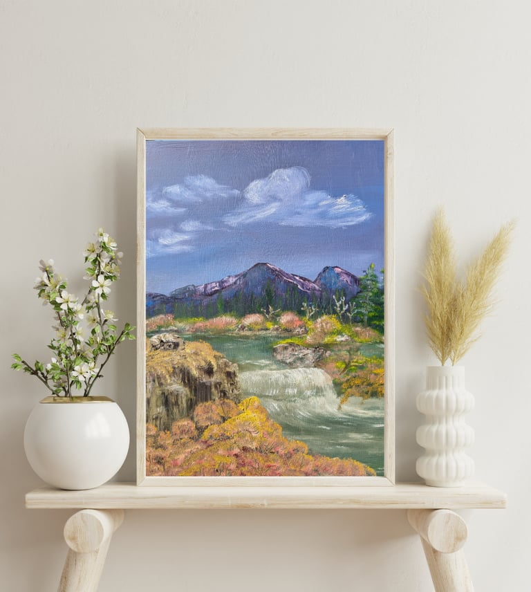Framed oil painting of a scenic landscape with mountains, waterfall, and blue sky on a minimalist shelf.
