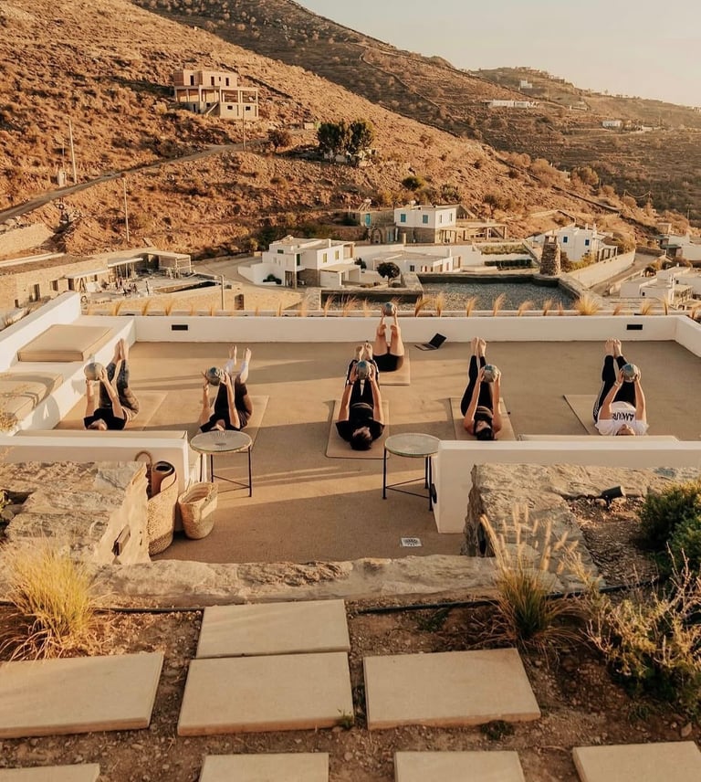 Group pilates class practicing on a sunny rooftop terrace overlooking a scenic mountain valley.