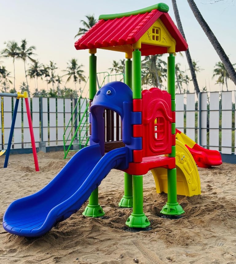 Colorful outdoor plastic playground equipment with a blue slide on a sandy beach under palm trees.