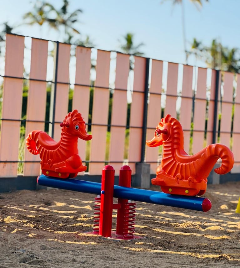 A bright orange seahorse seesaw on a sandy playground with tropical palm trees in the background.
