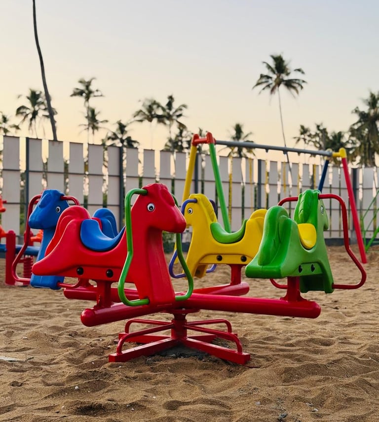 Colorful horse-shaped roundabout on a sandy playground with palm trees in the background.