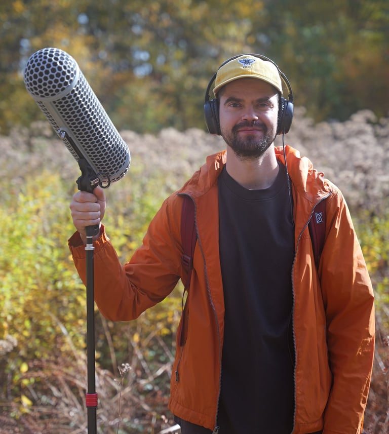 Gene Chaban, freelance sound designer and field recordist, smiling outdoors with a boom mic and head
