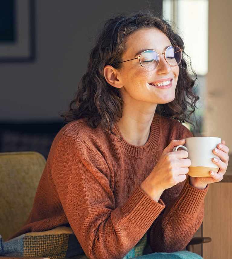 a woman in glasses and a sweater is smiling and holding a cup of coffee after individual counselling