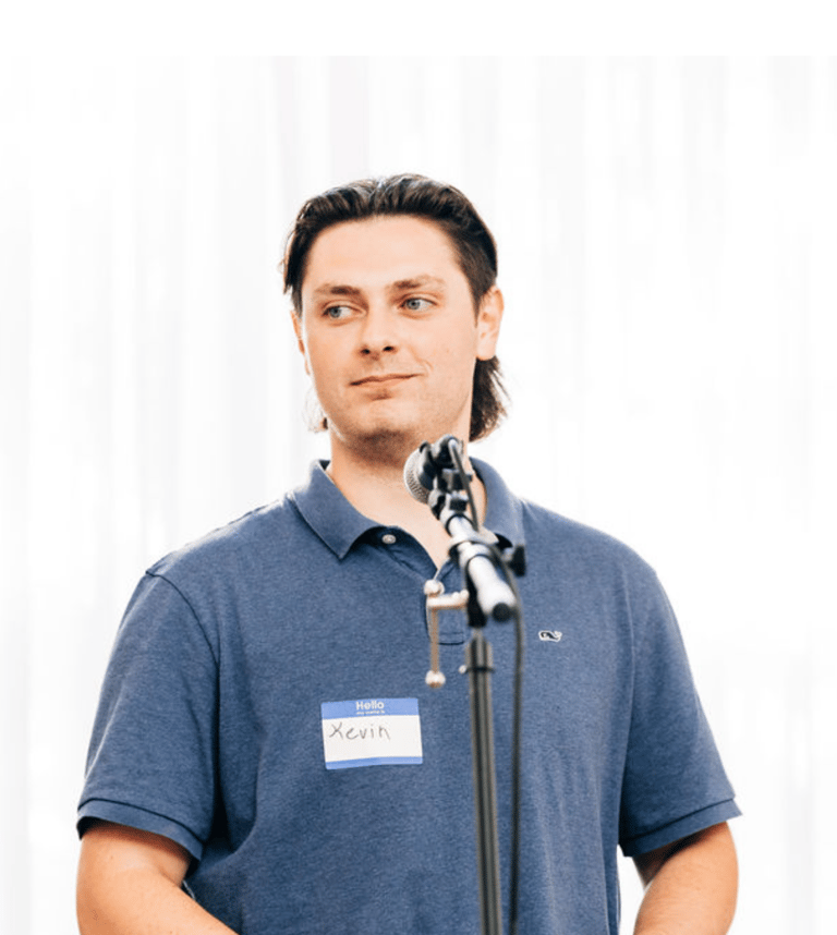 Kevin Bockius wearing a collared shirt, standing in front of a microphone giving a speech