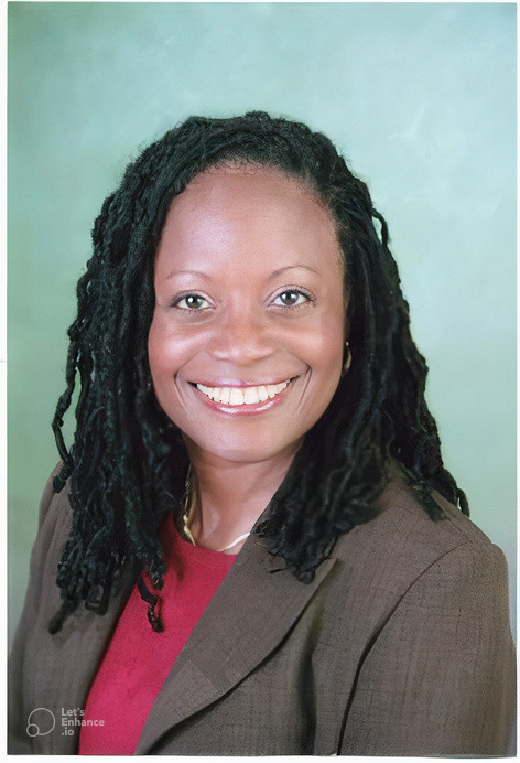 Professional portrait of a smiling woman with long dreadlocks wearing a brown blazer.