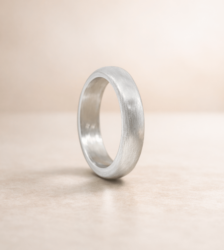 A brushed matte 999 fine silver wedding band standing vertically on a neutral beige background.